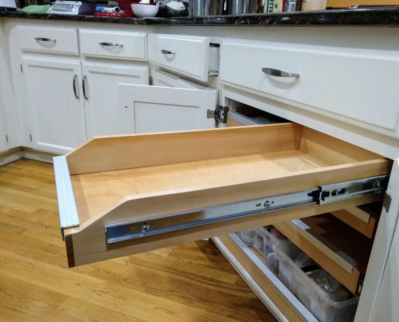 A woodworking project showing a kitchen cabinet with an open drawer featuring neatly organized utensils
