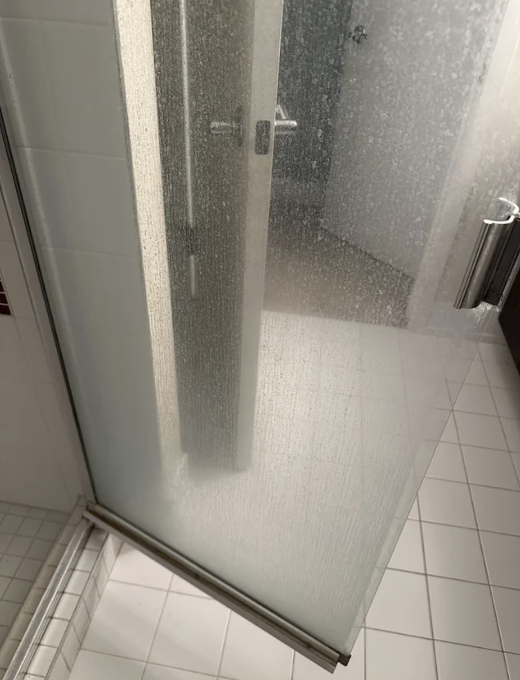 Glass shower door half open showing a tiled shower interior