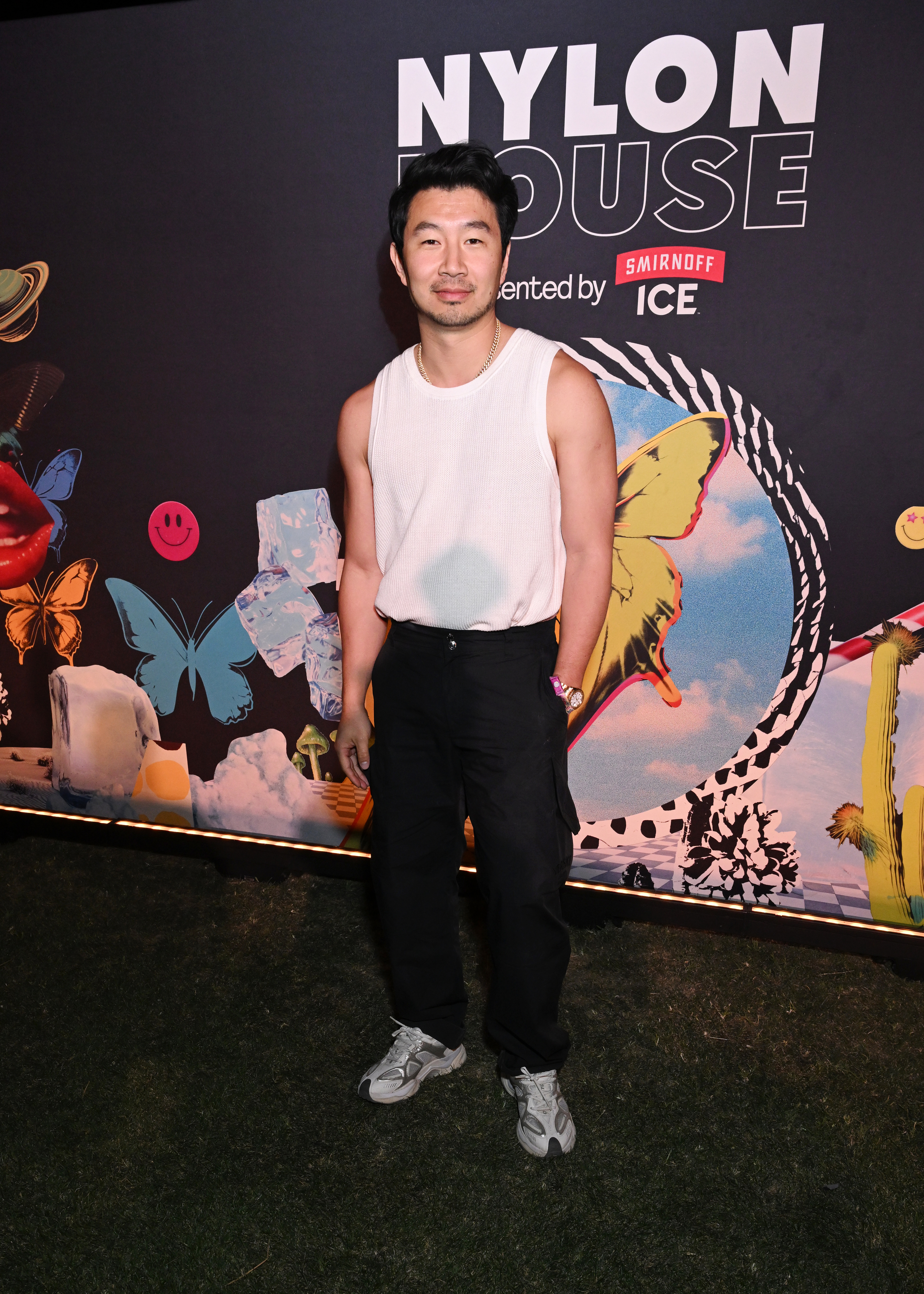 Man in sleeveless top and pants stands before event backdrop with decorative elements