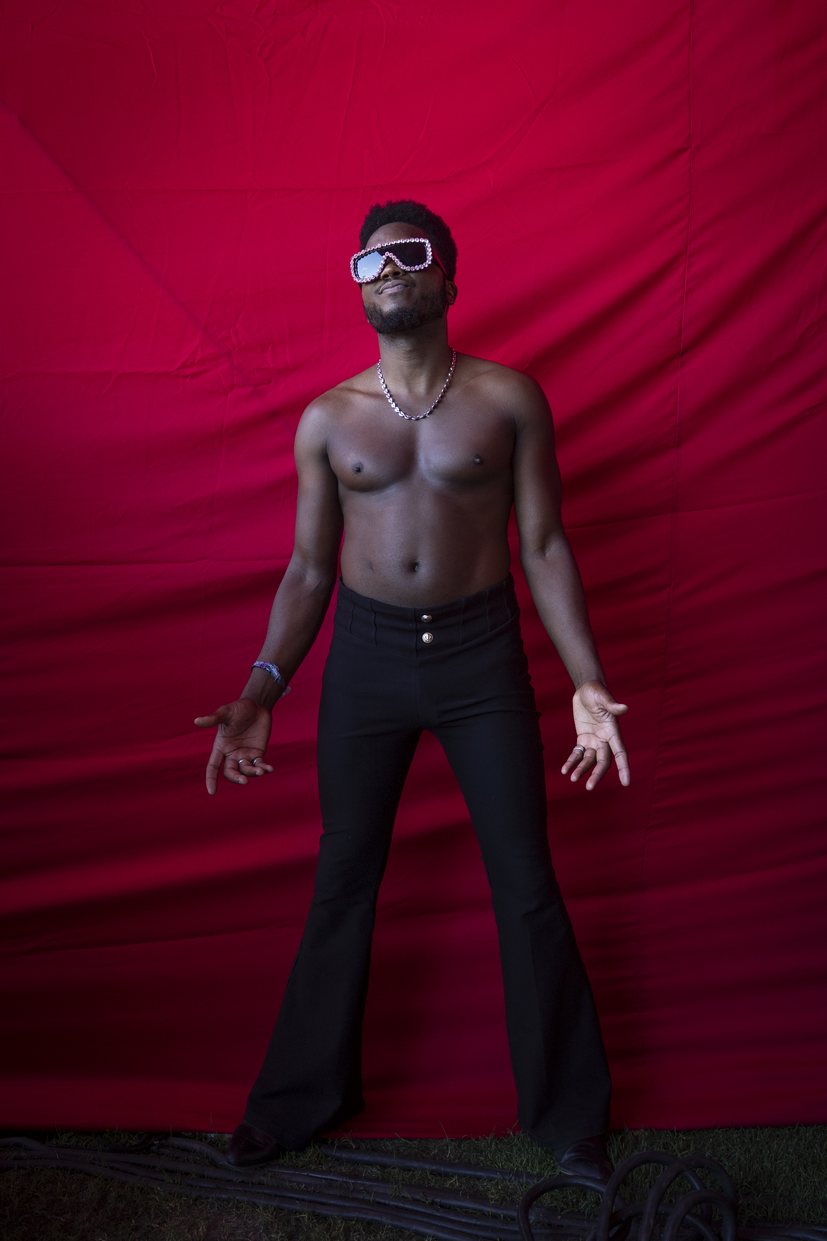 Man with sunglasses and black pants posing against red backdrop