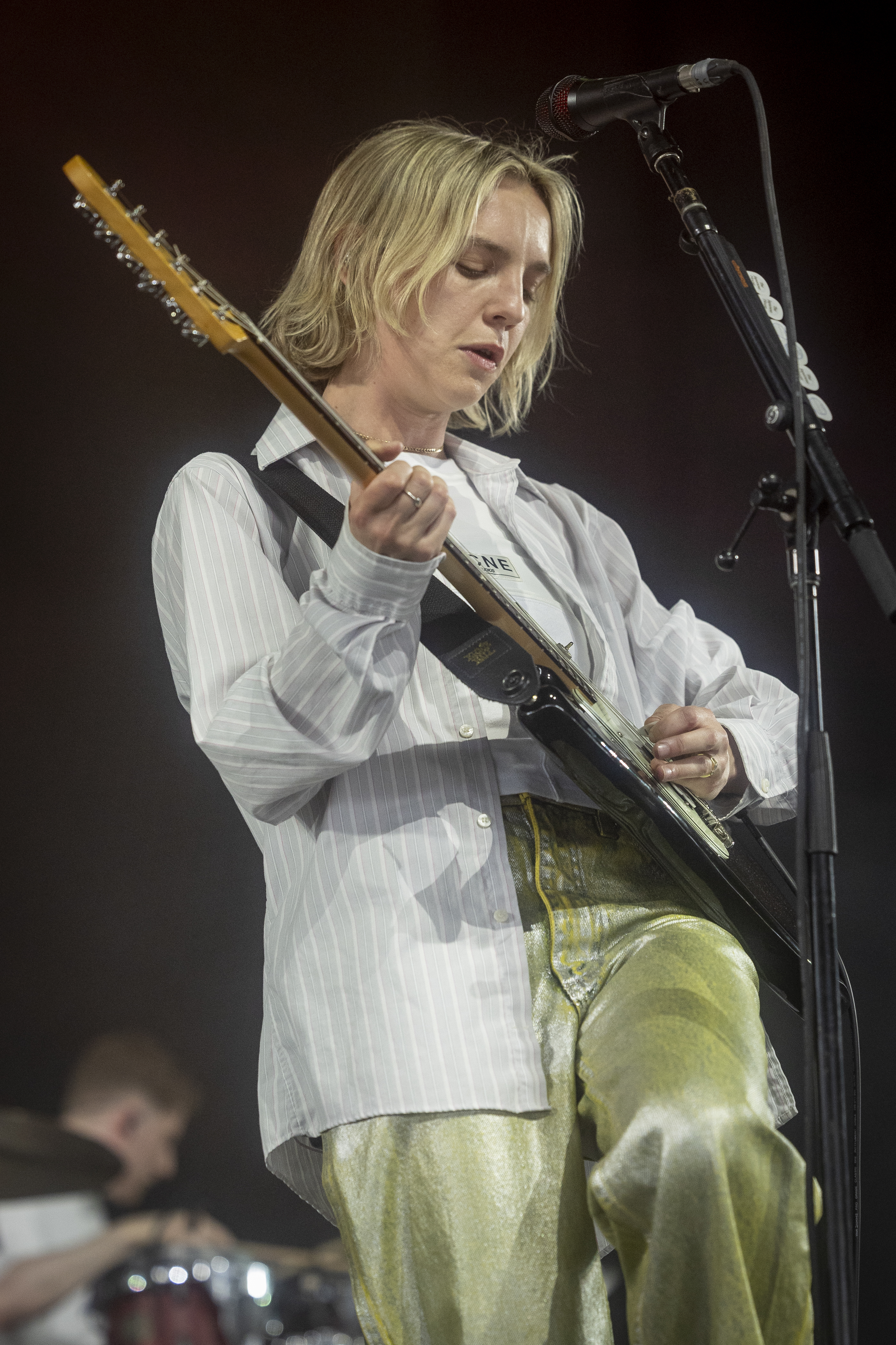 Person playing guitar onstage wearing a striped shirt and metallic trousers