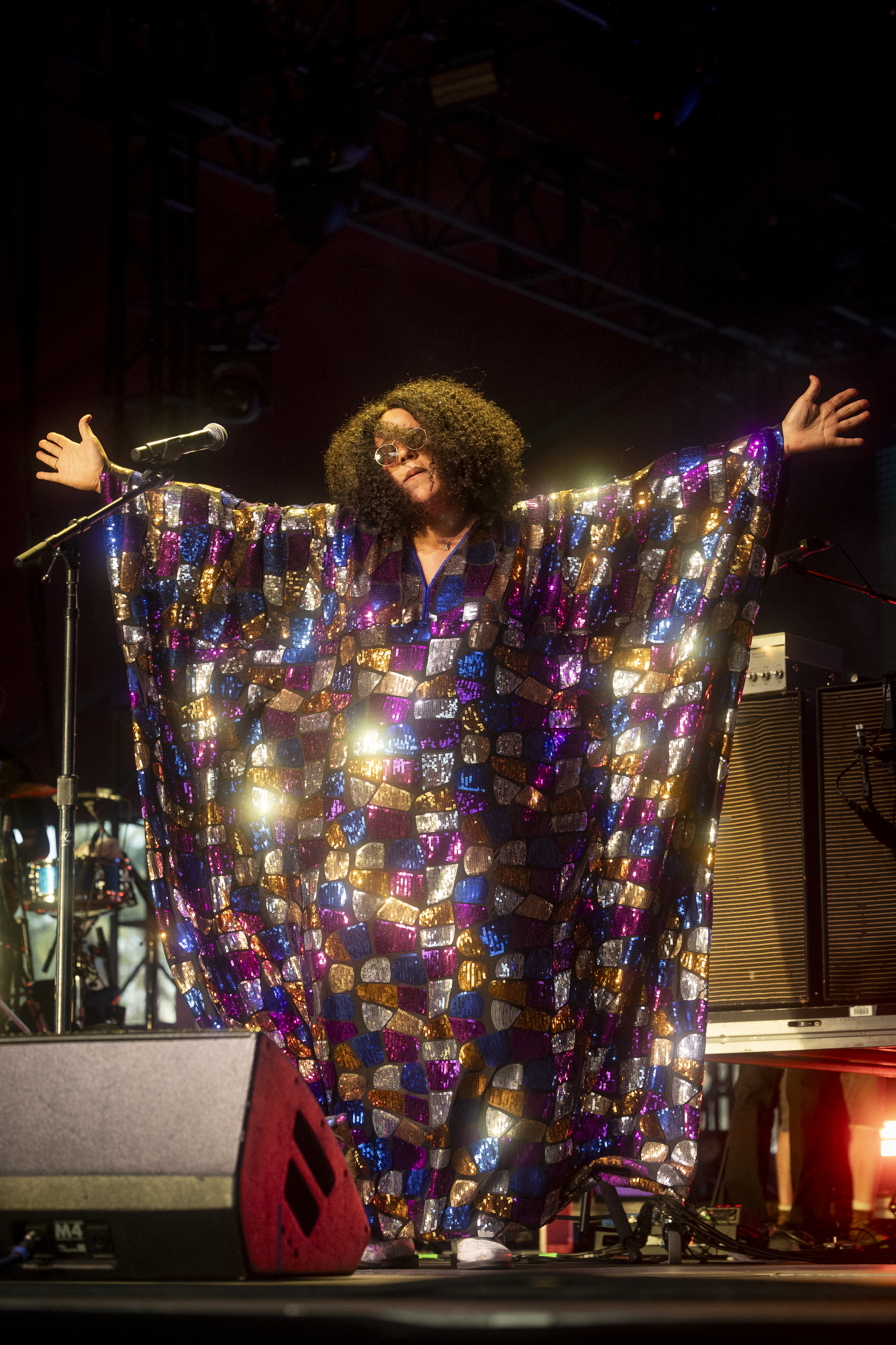 Performer in an oversized, patterned cape with arms outstretched on stage