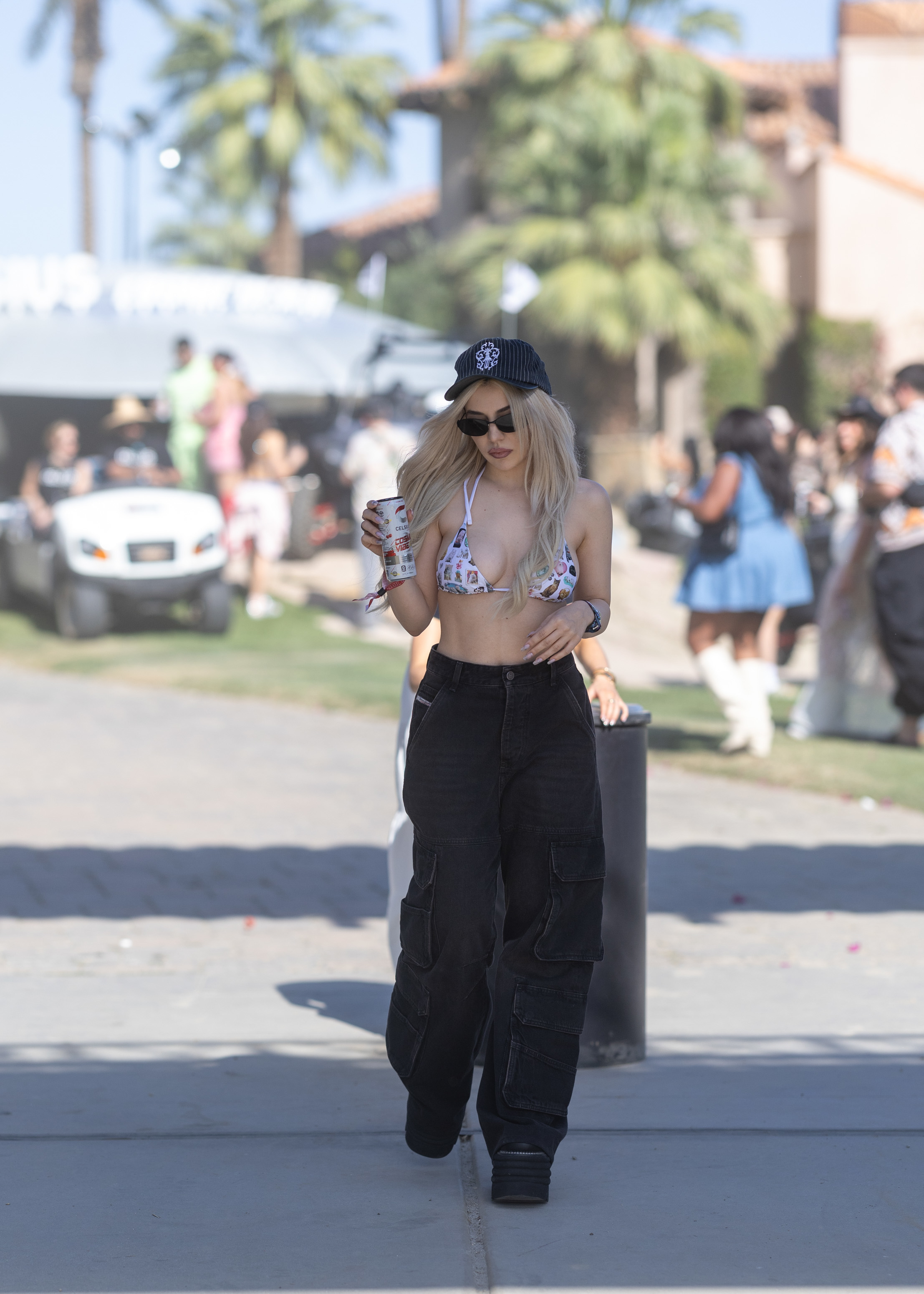 Person in a beanie and high-waisted pants holding a drink and phone, walking outdoors