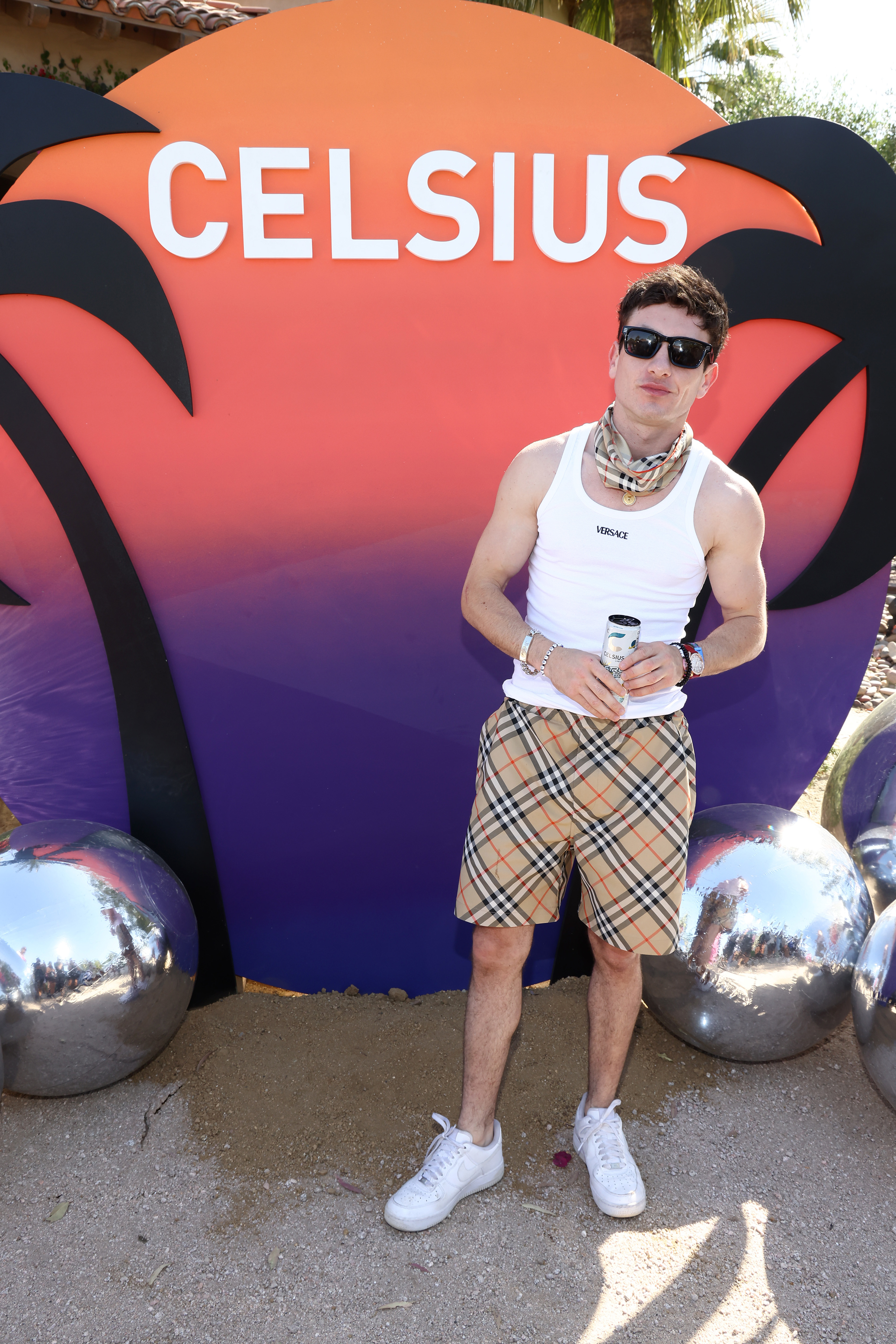 Man in white tank top and plaid shorts standing in front of a Celsius banner with silver spheres nearby