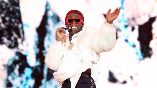 Lil Uzi Vert performing on stage with microphone, wearing fluffy jacket, sunglasses, and headband