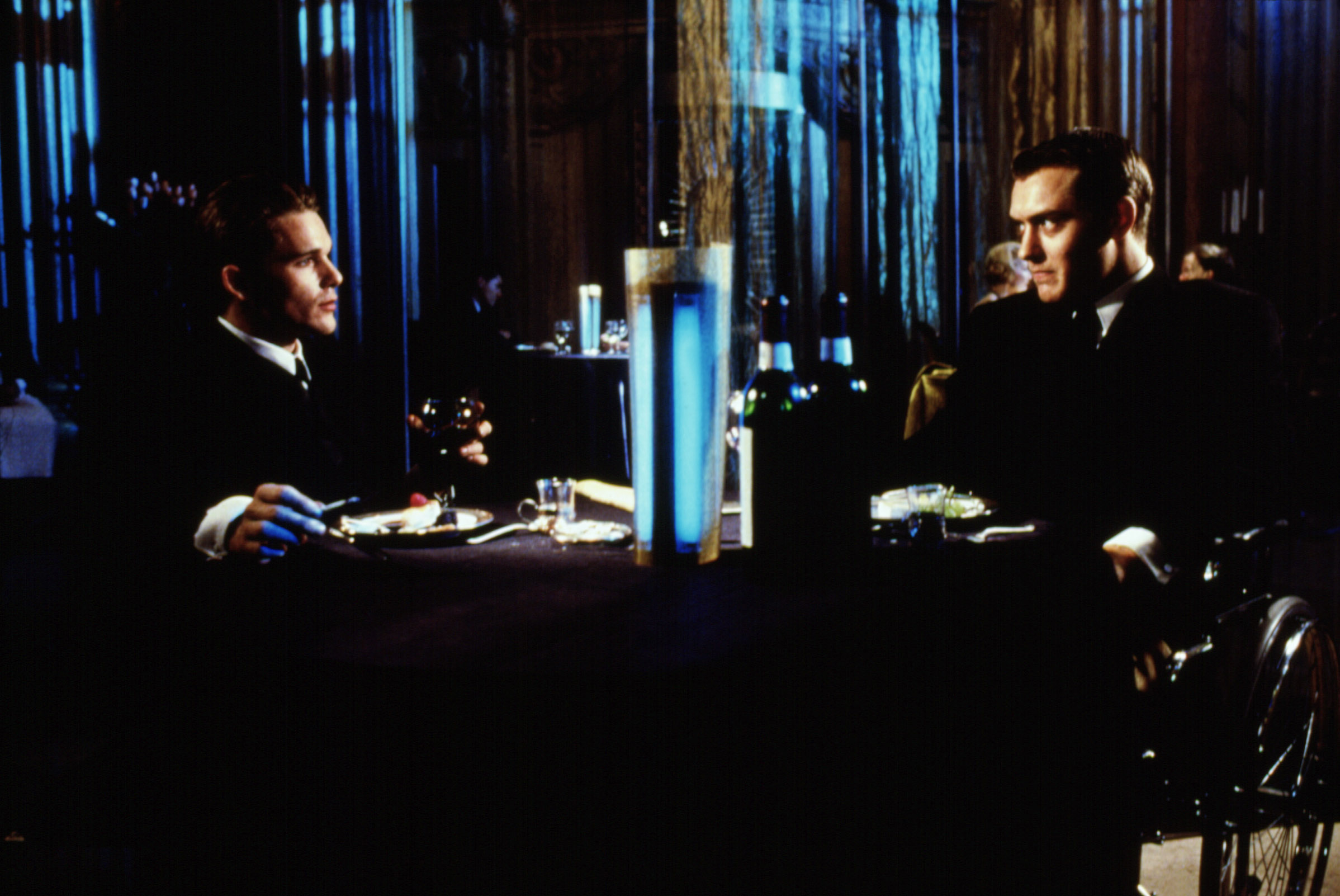 Two characters in formal attire sit at a dining table in a scene from a film