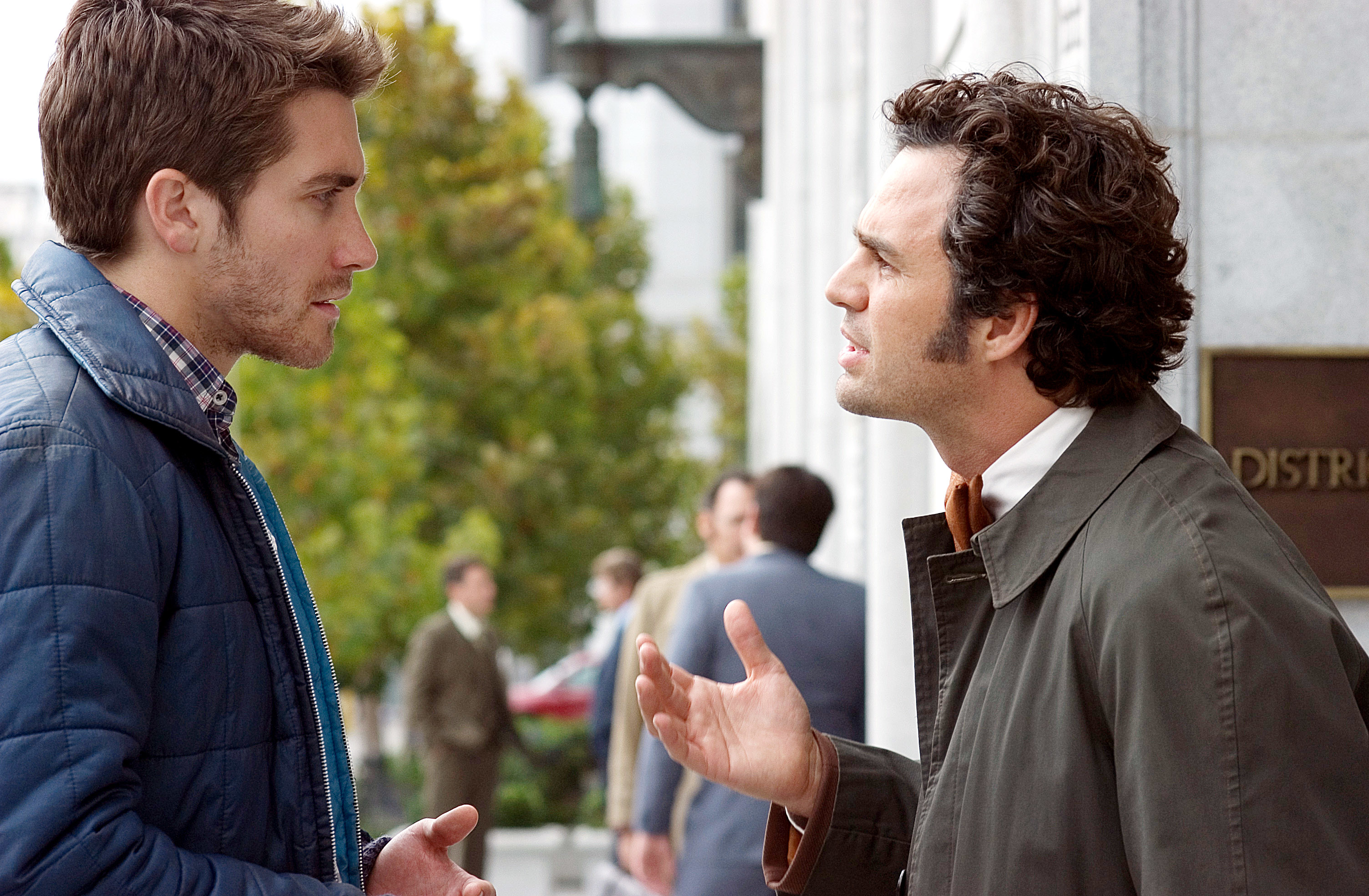 Two men in casual jackets have a conversation on a city street