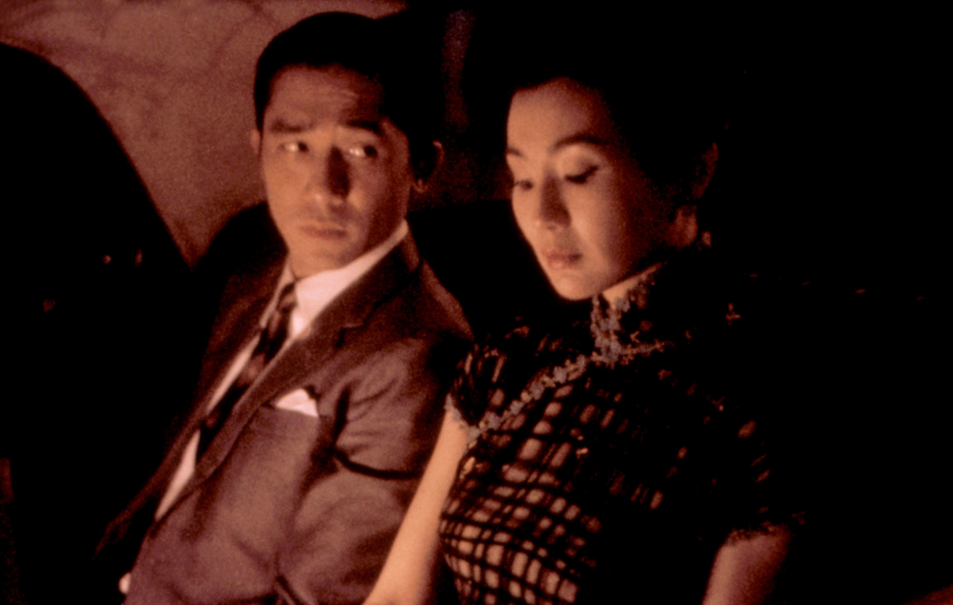 A man in a suit and a woman in a cheongsam sit close together, conveying a sense of intimacy or tension