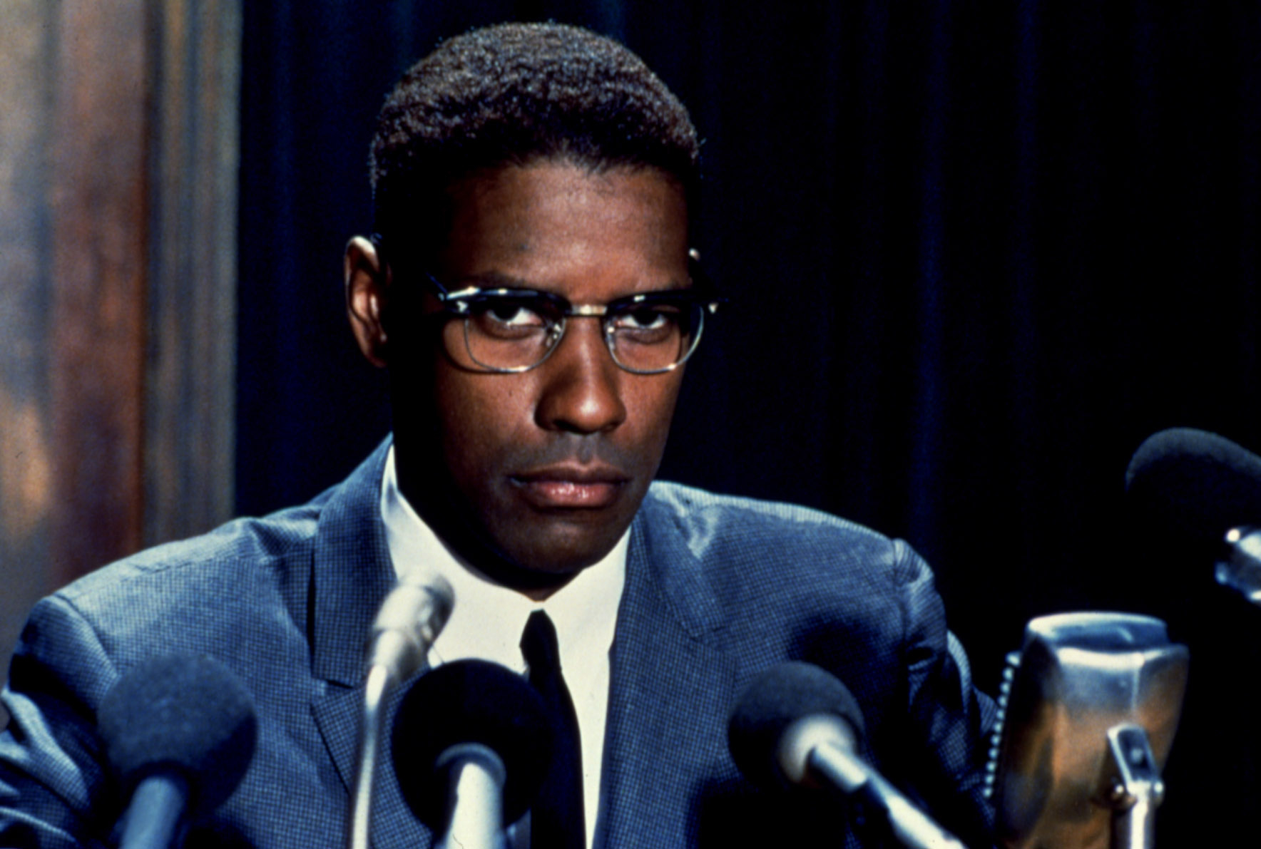 Actor Denzel Washington portraying Malcolm X in a suit at a podium in the film &quot;Malcolm X.&quot;
