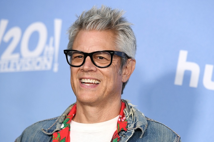 Man smiling in glasses, wearing a jacket with floral print and denim trim