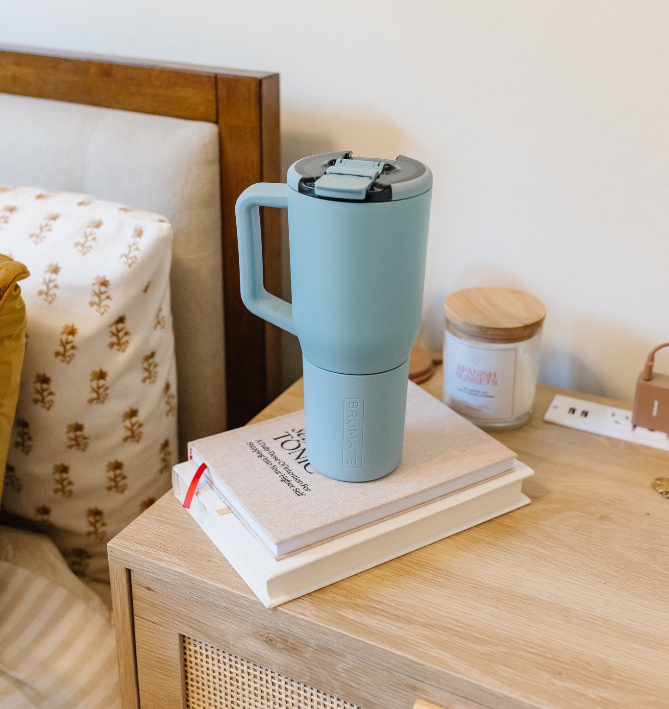 Insulated travel mug on books beside a bed, ideal for a cozy read or morning routine