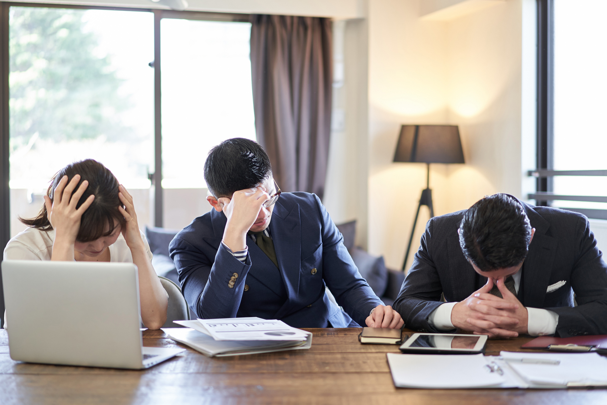 デスクで頭を抱える３人のビジネスパーソンがストレスを感じている様子。