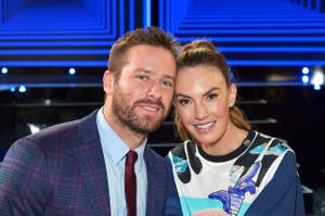 Armie Hammer and Elizabeth Chambers smiling closely at an event; Hammer in a plaid suit, Chambers in a graphic dress