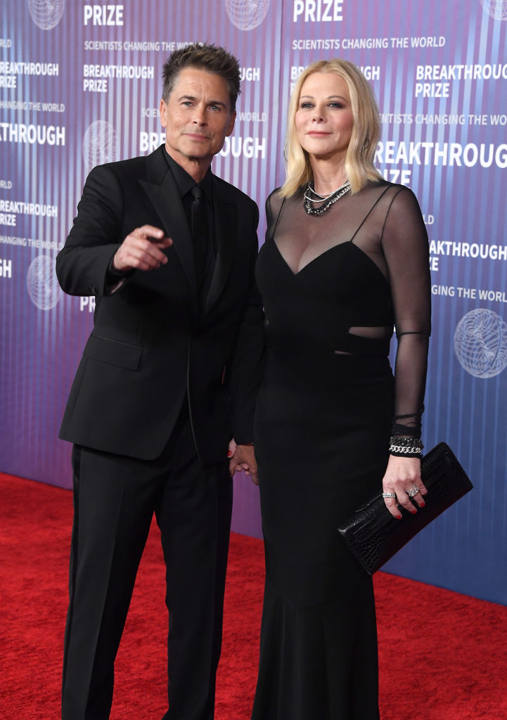 Rob Lowe and Sheryl Berkoff posing together on red carpet, Rob in a suit and Sheryl in a black dress with sheer details