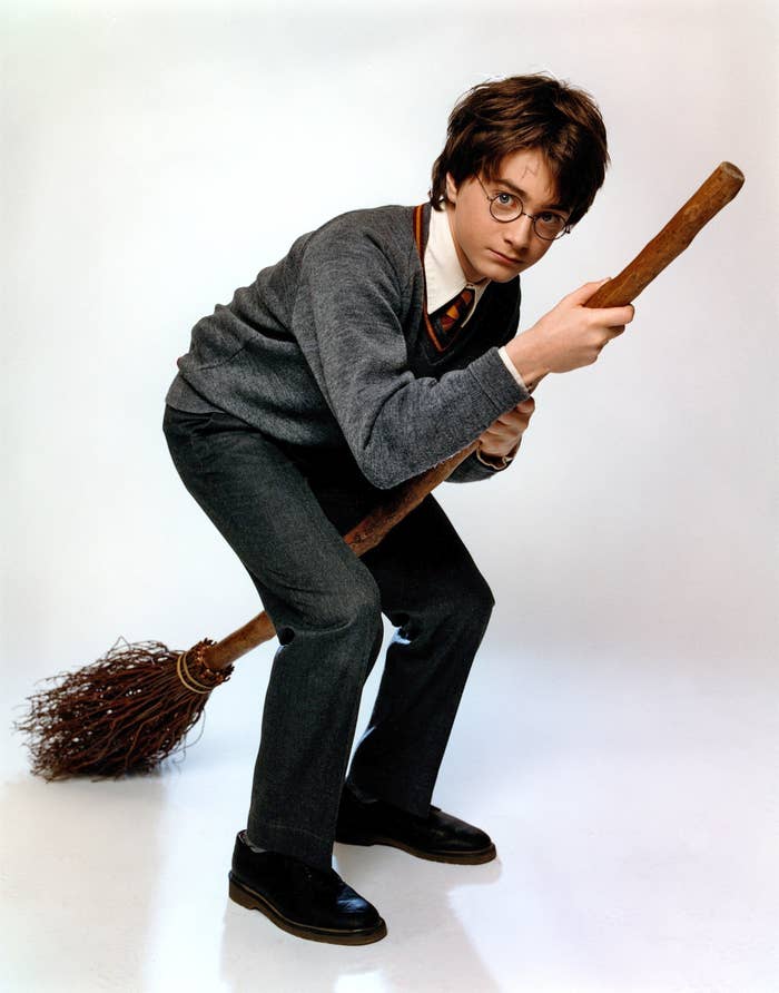 Harry Potter character posing with a wand and broomstick, in Hogwarts uniform