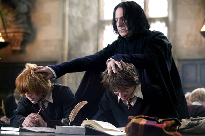 Severus Snape stands behind Ron Weasley and Harry Potter, placing his hand on their heads in a classroom setting