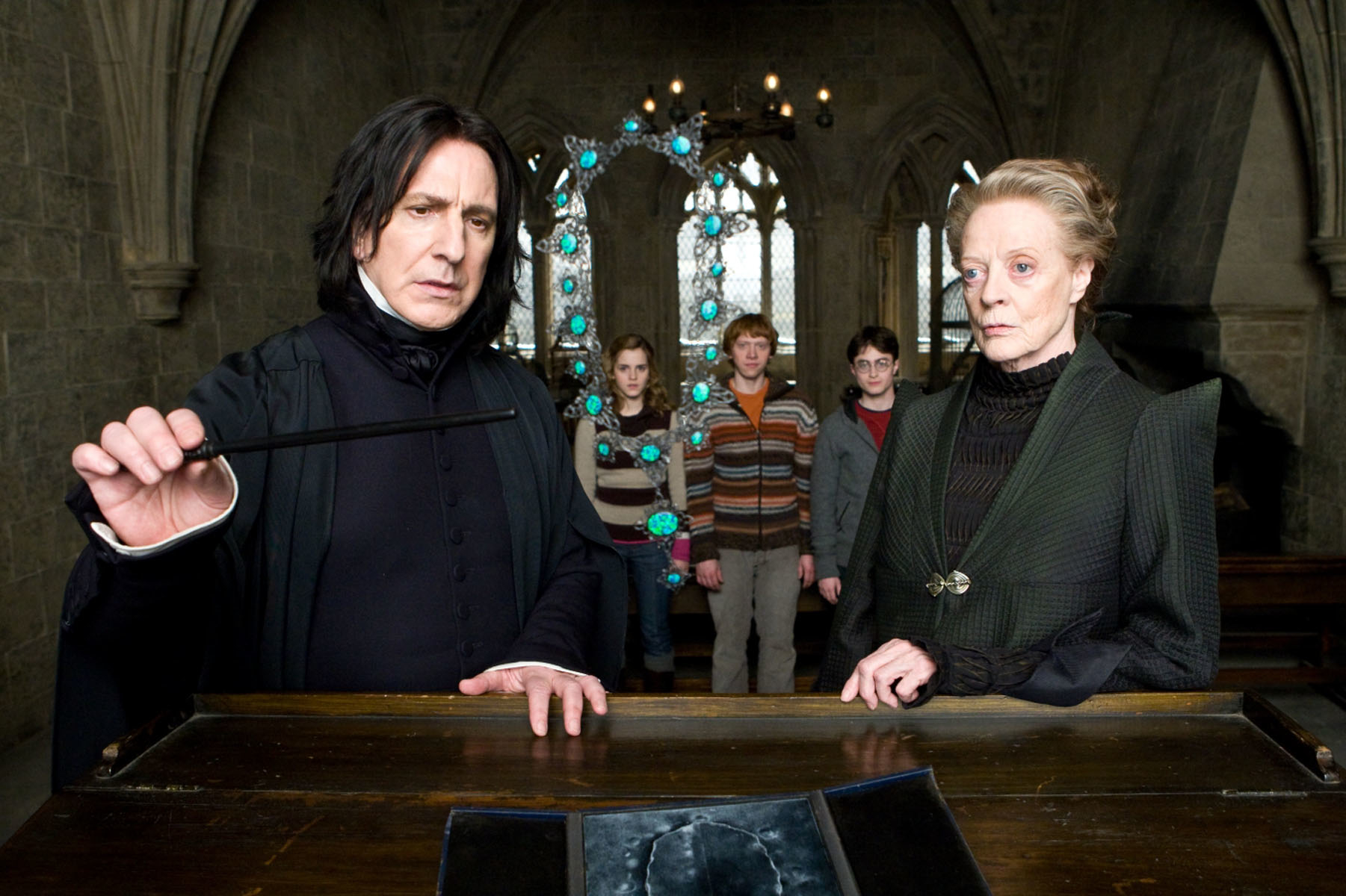 Severus Snape and Minerva McGonagall in Hogwarts attire standing, three students behind them looking serious