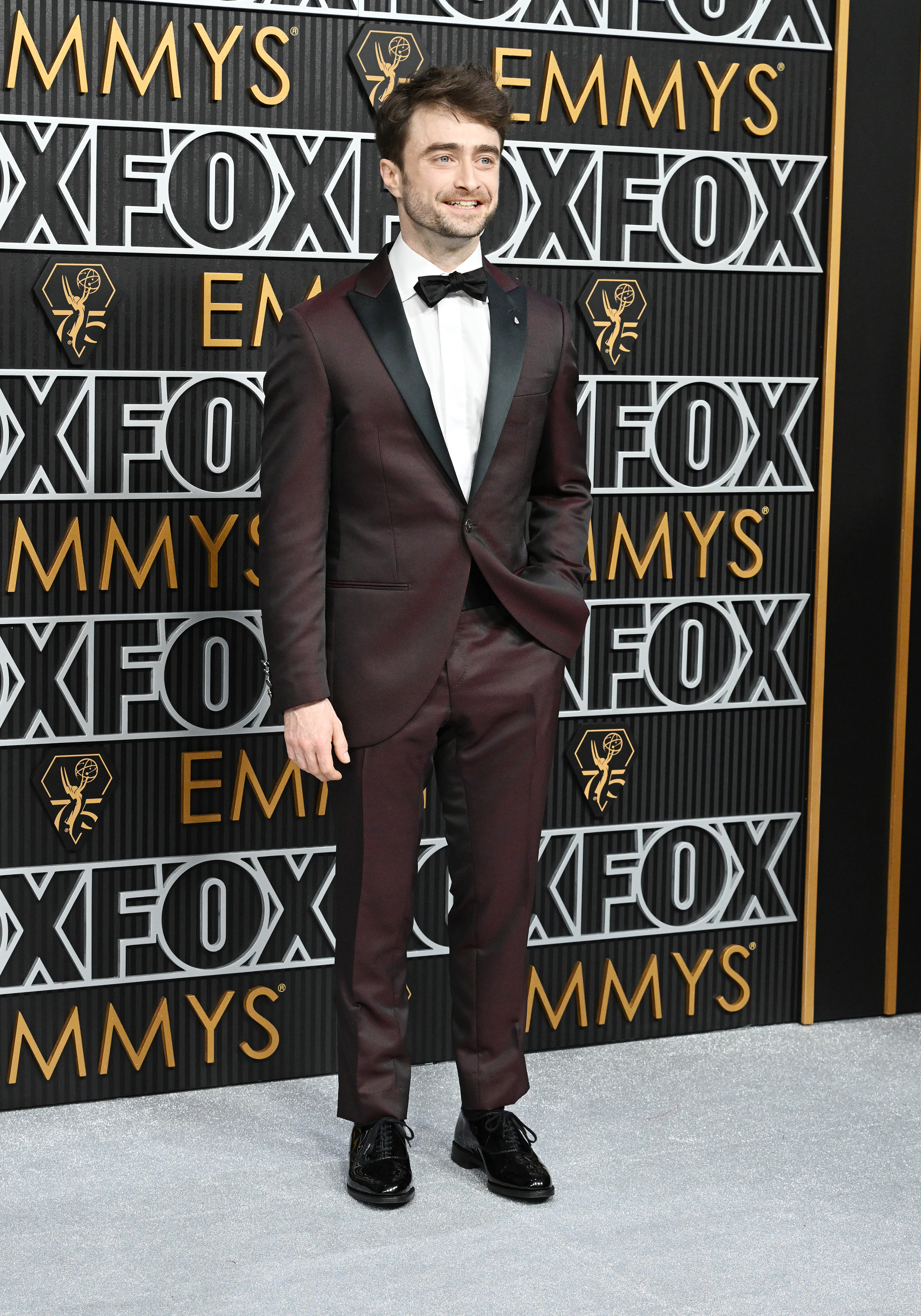 Daniel Radcliffe in a dark suit with a bowtie at the Emmys backdrop