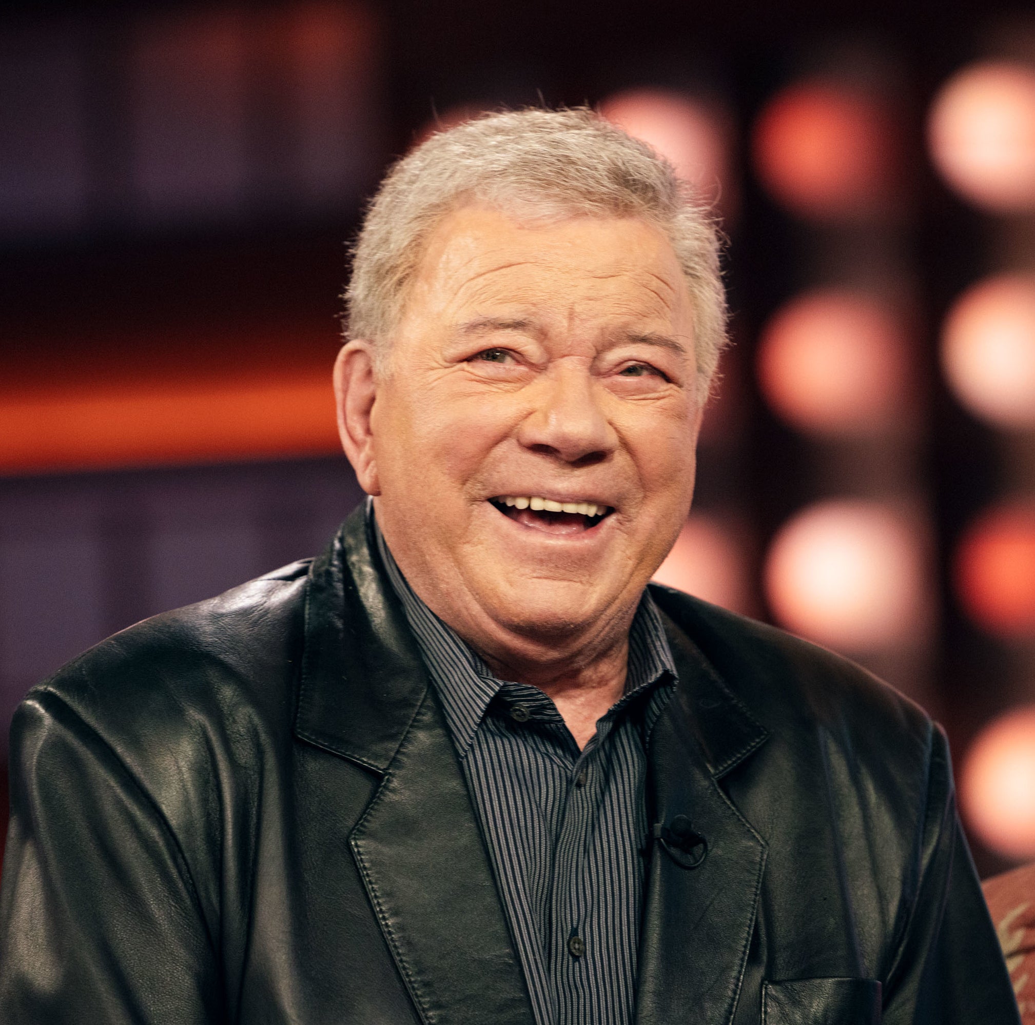 Smiling person in a leather jacket seated during an interview