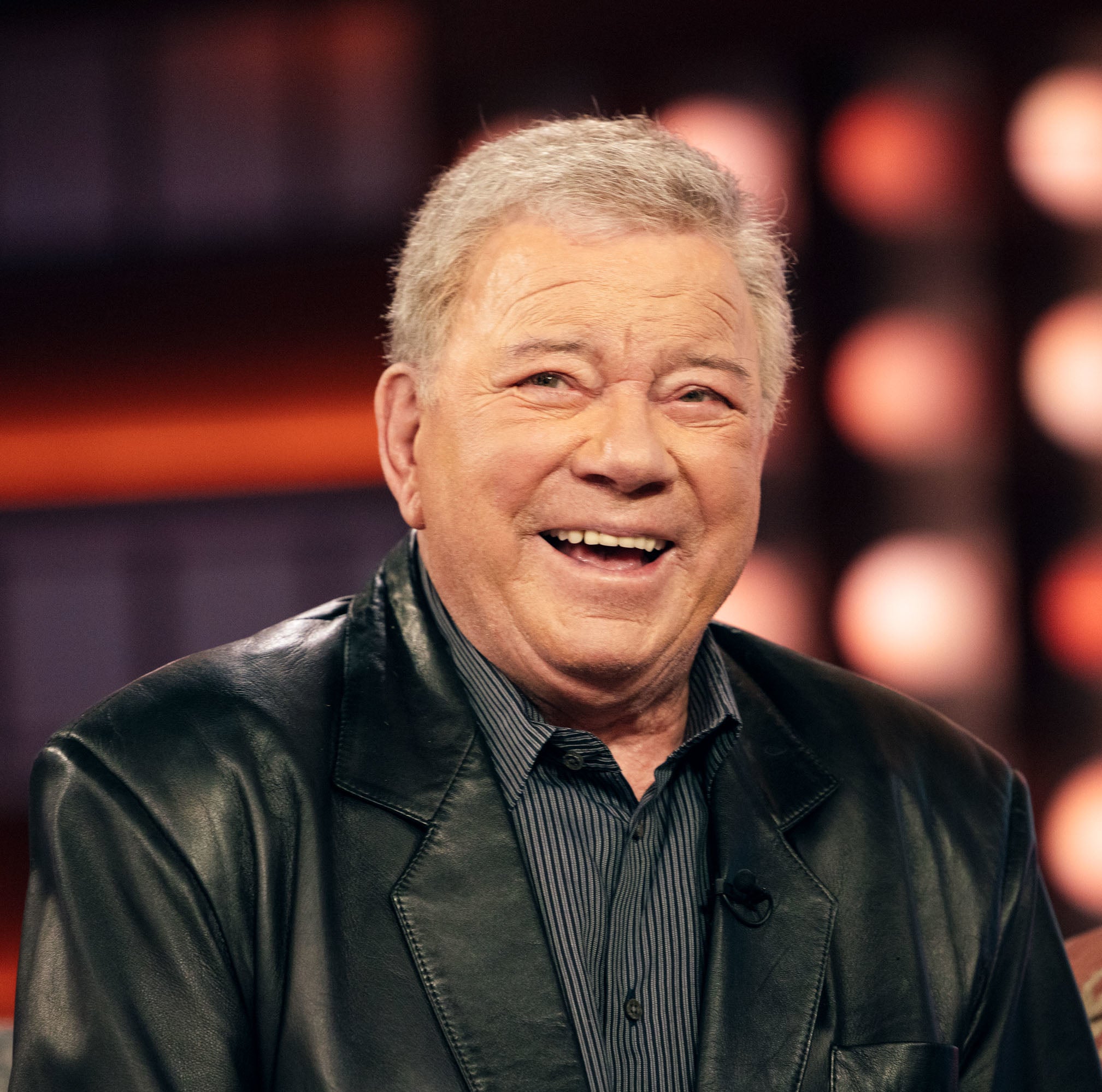Smiling person in a leather jacket seated during an interview