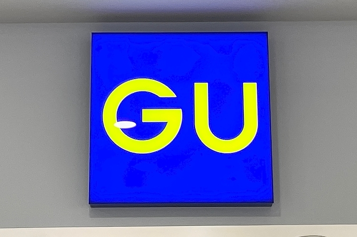 Sign with the letters “GU” on a blue background, mounted on a wall above some fixtures