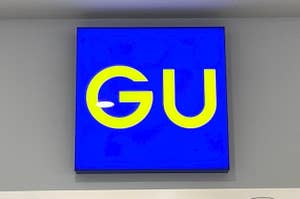 Sign with the letters "GU" on a blue background, mounted on a wall above some fixtures