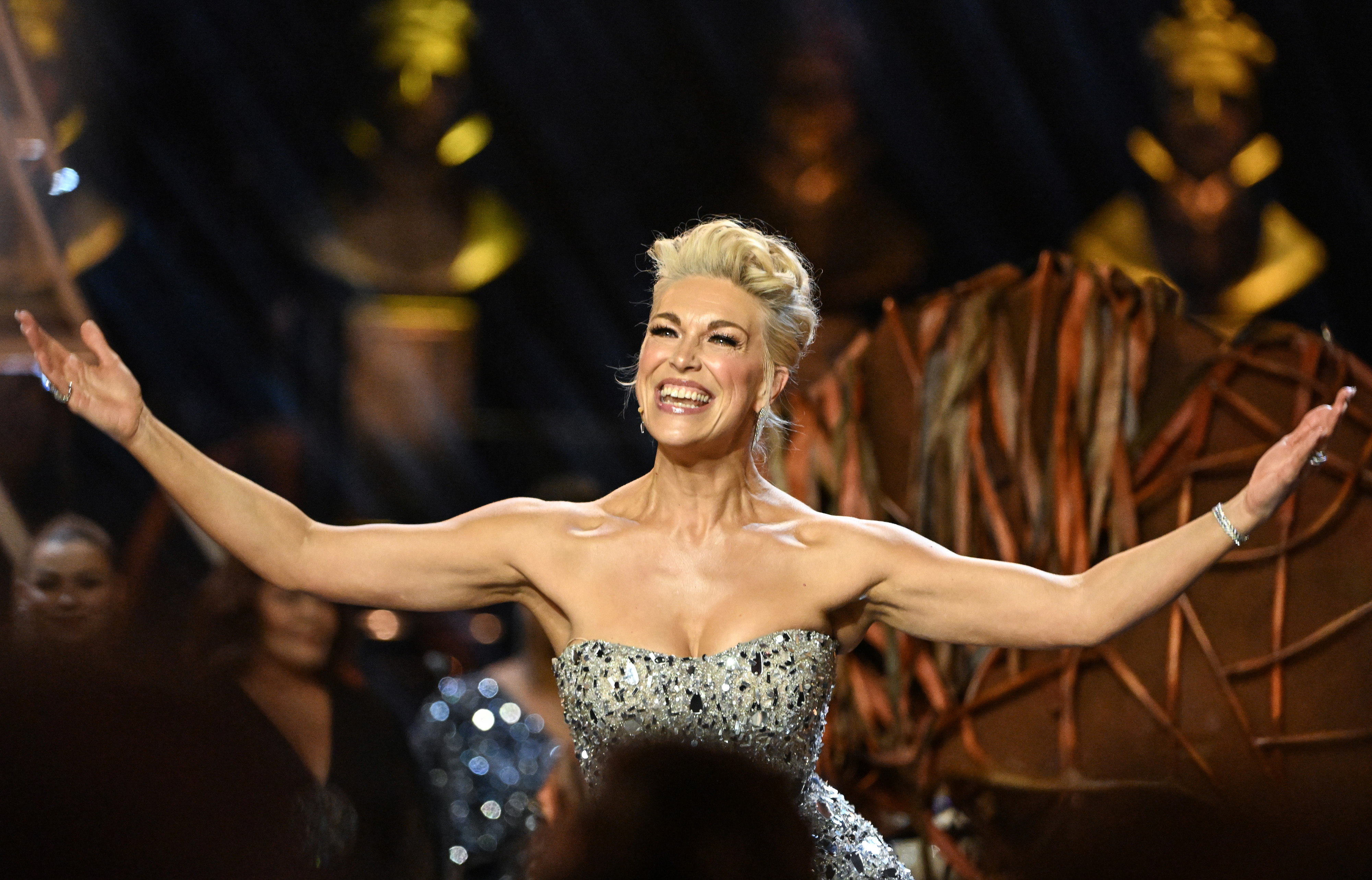 Hannah Waddingham on stage with arms outstretched, wearing a strapless, embellished gown, expressing joy
