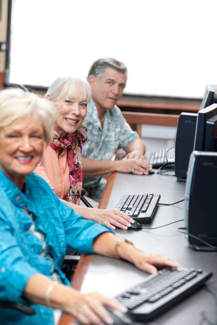 Three smiling senior adults using computers in a classroom setting