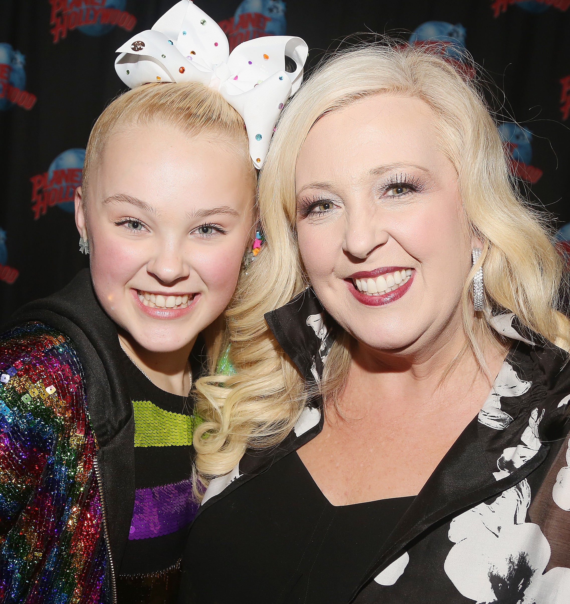 JoJo Siwa in a sequined top posing with her mother, Jessalynn Siwa, who wears a floral top