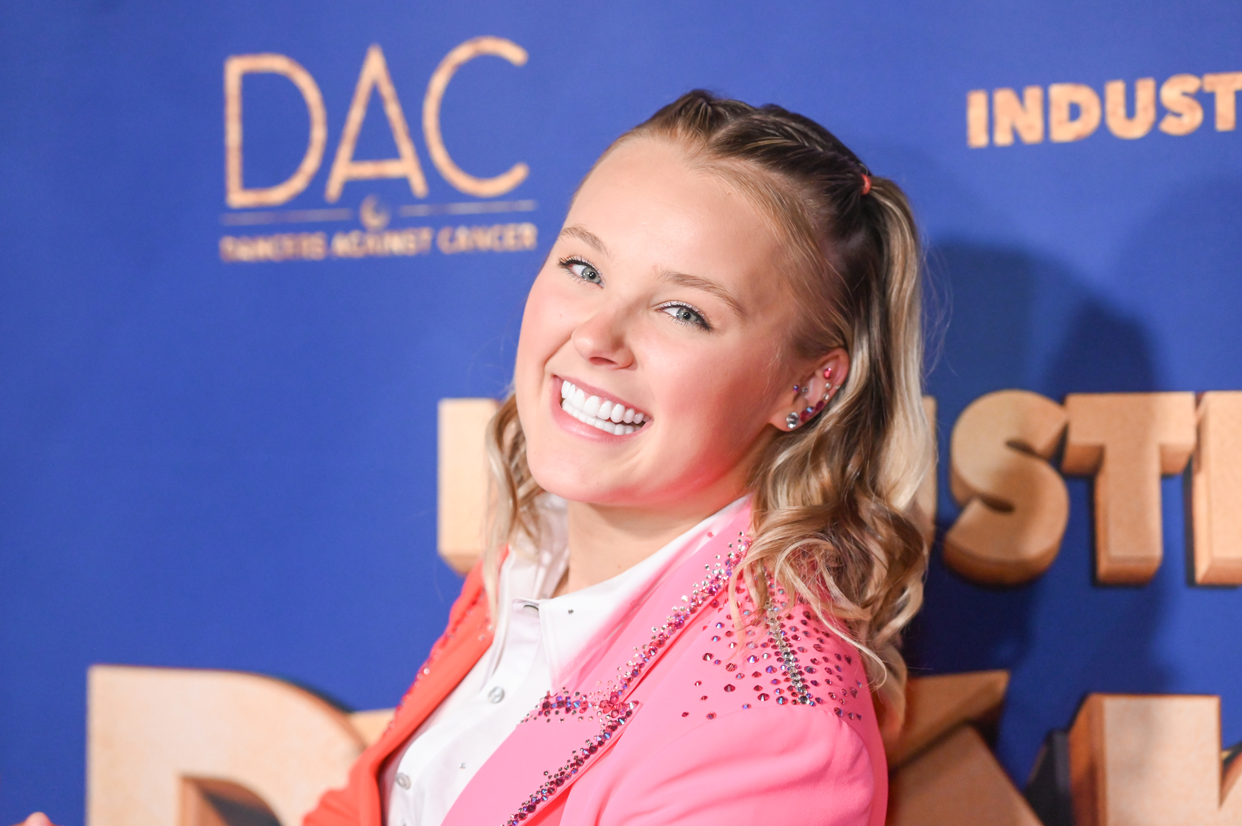JoJo Siwa smiling at a premiere event, wearing a pink blazer over a white shirt