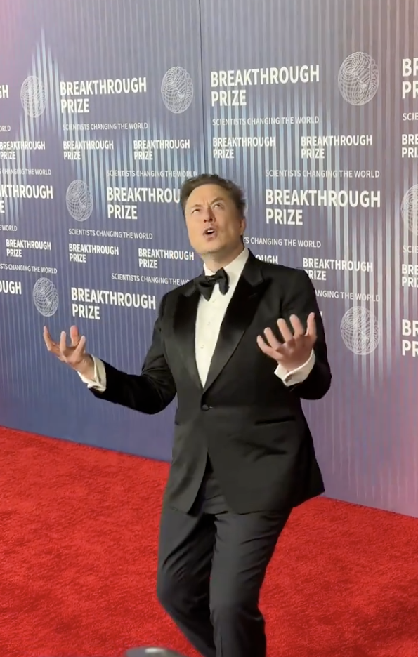Elon Musk in a tuxedo with hands up, making a surprised expression at the Breakthrough Prize event