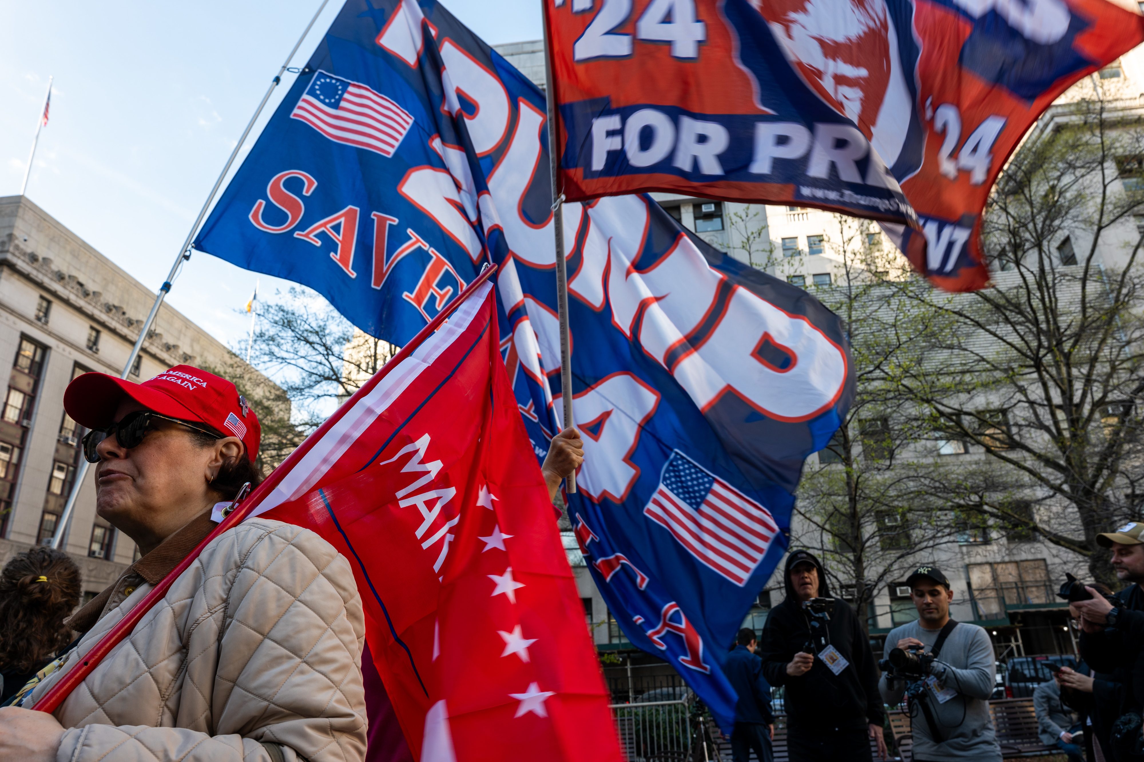 Supporters with &quot;Trump 2024&quot; flags at a rally, one wearing a red hat