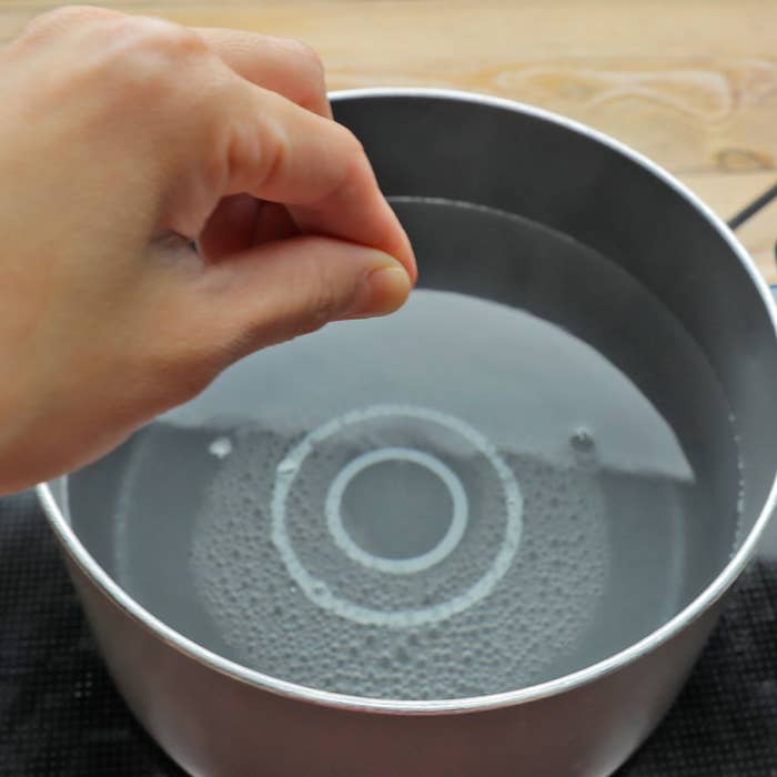 鍋に水を指で触れる人の手
