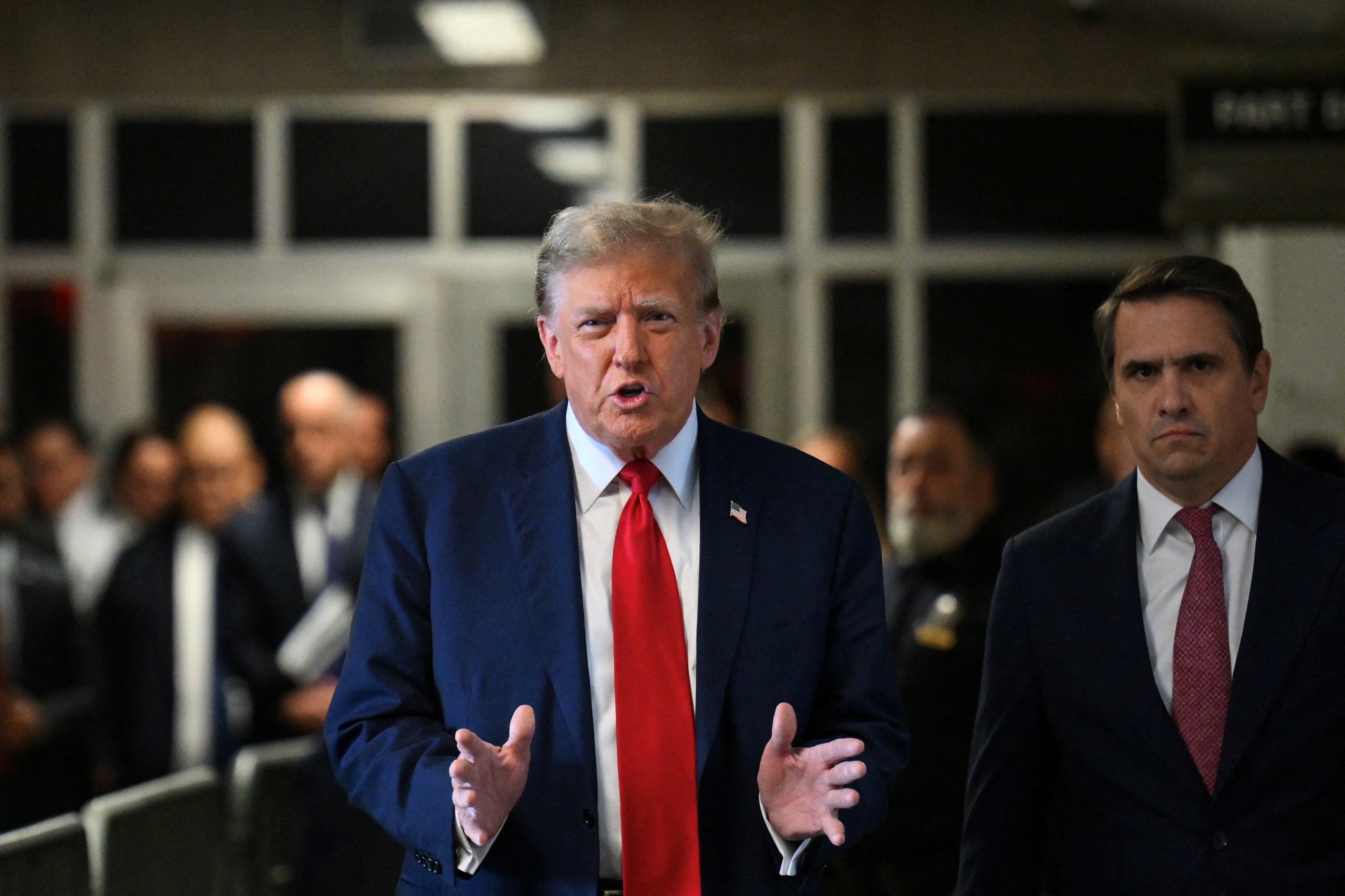 Donald Trump in suit with red tie walks with an unidentified man in the background