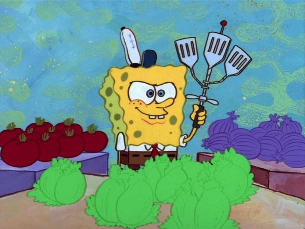 SpongeBob in square pants holding a spatula with tomatoes and lettuce on a table