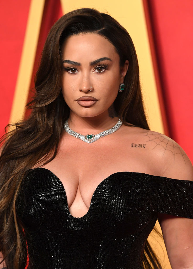 Demi Lovato wearing a black sequined dress and emerald necklace, looking at the camera