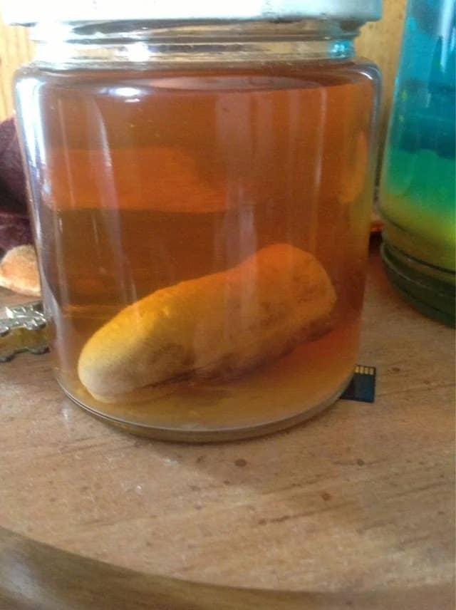 A severed thumb submerged in a jar of liquid with miscellaneous items in the background
