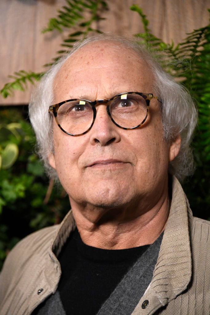 Close-up of Chevy Chase with grey hair, wearing glasses and a beige jacket