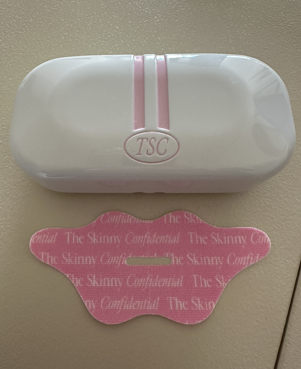 A TSC branded case with a matching lip-shaped face tape below it, both with &quot;The Skinny Confidential&quot; text