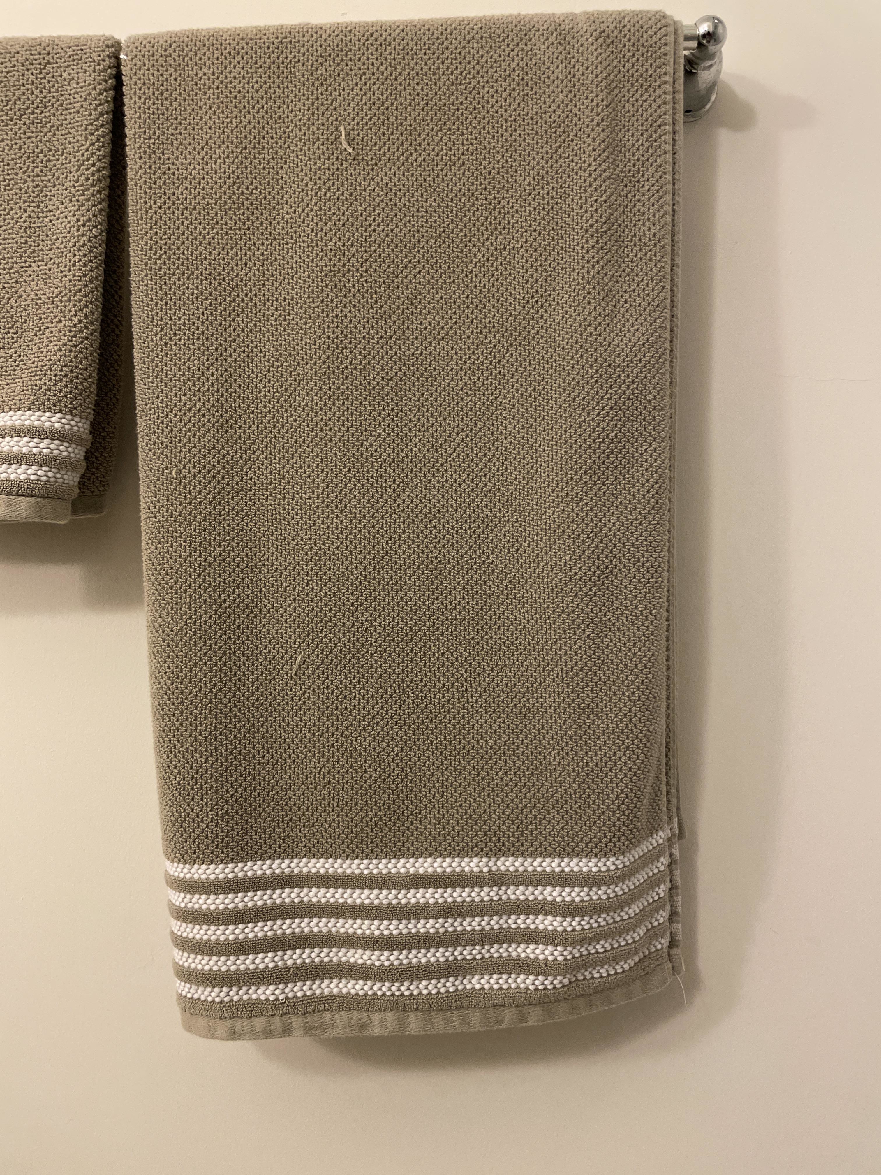 Beige towel hanging on a rack with decorative white stripes at the bottom