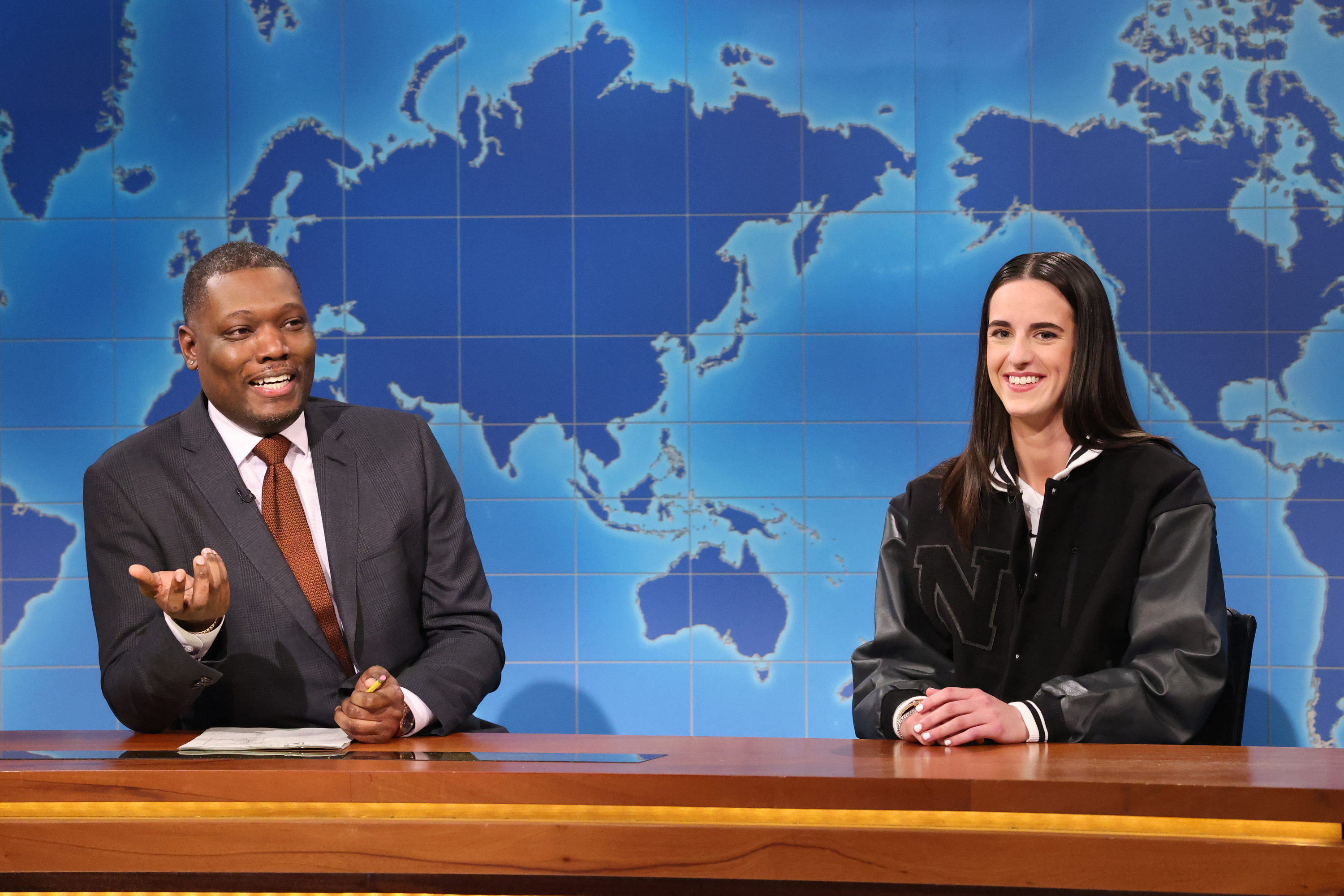 Michael Che and a Caitlin Clark are sitting at the &quot;Weekend Update&quot; desk on the set of Saturday Night Live