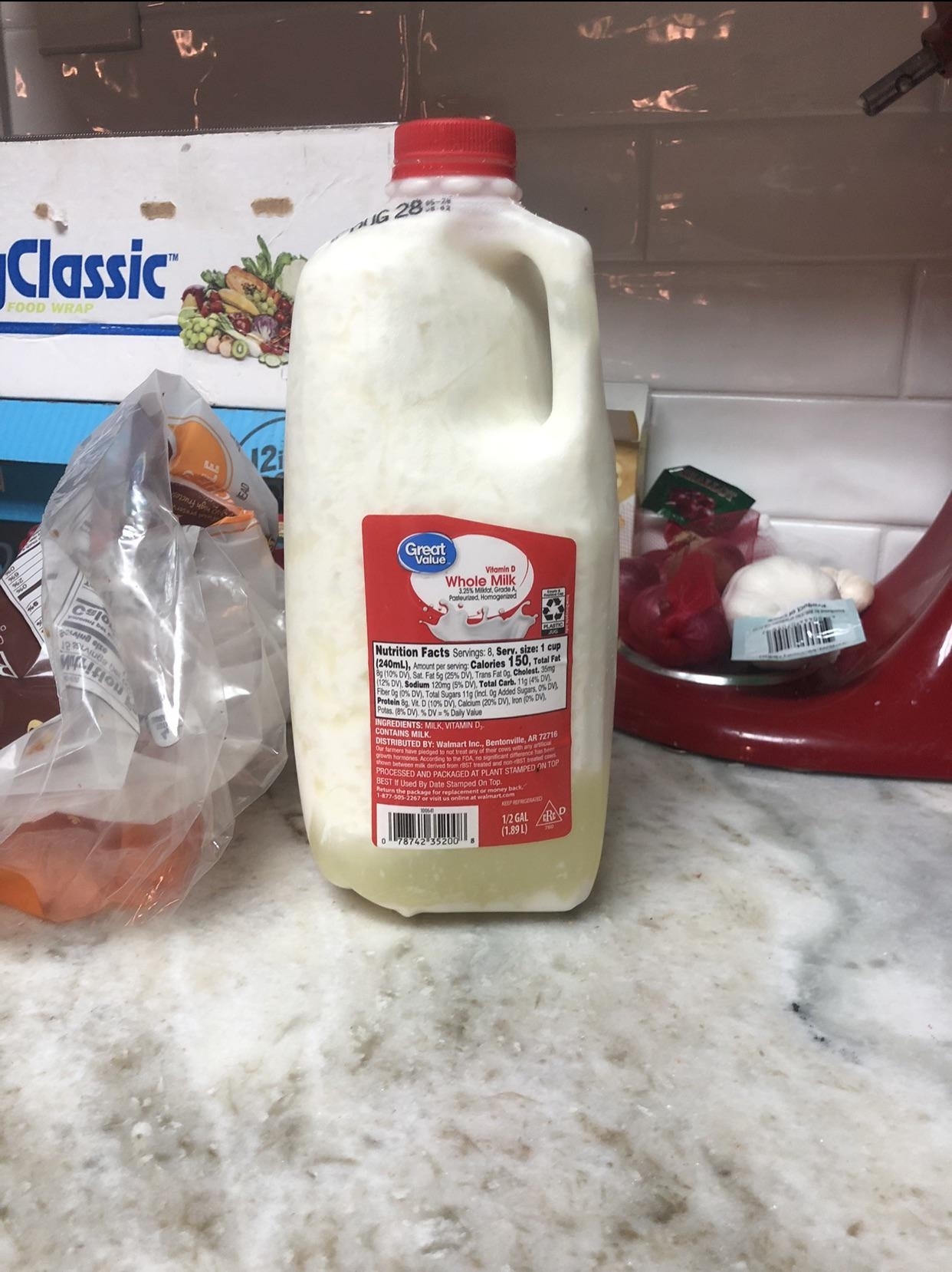 A gallon of expired whole milk on a kitchen counter with various groceries in the background