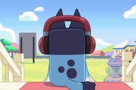 Blue cartoon character with headphones sitting on a porch