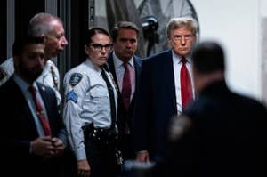 Former President Donald Trump walking with security personnel in a dimly lit corridor