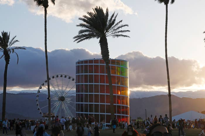 Spectacular view at sunset of a ferris wheel and colorful, cylindrical structure at a festival with mountains in backdrop