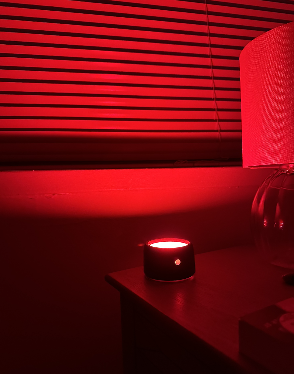 Smart speaker on a bedside table illuminated by red light, creating a cozy atmosphere
