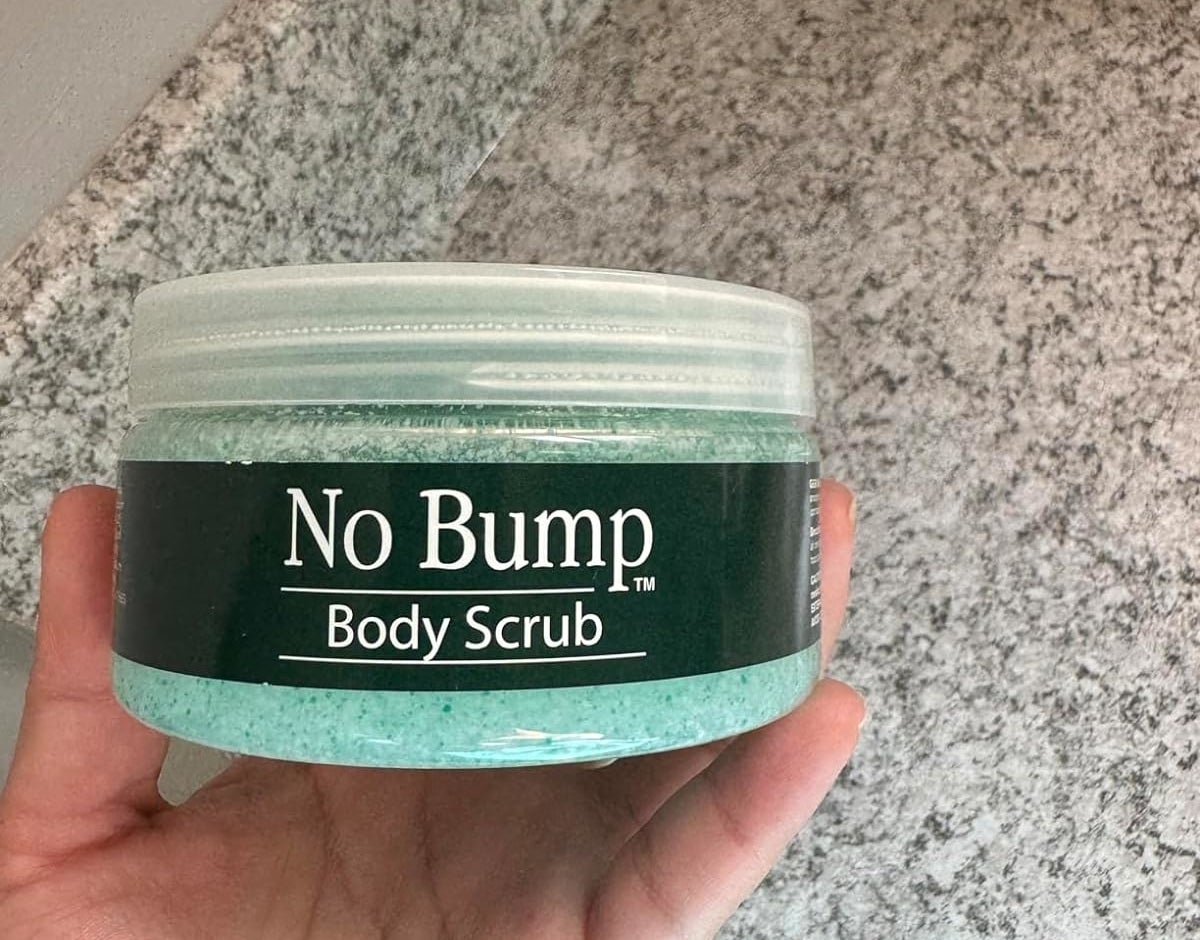 Reviewer&#x27;s photo of a hand holding a jar of &#x27;No Bump Body Scrub&#x27; against a marble counter background