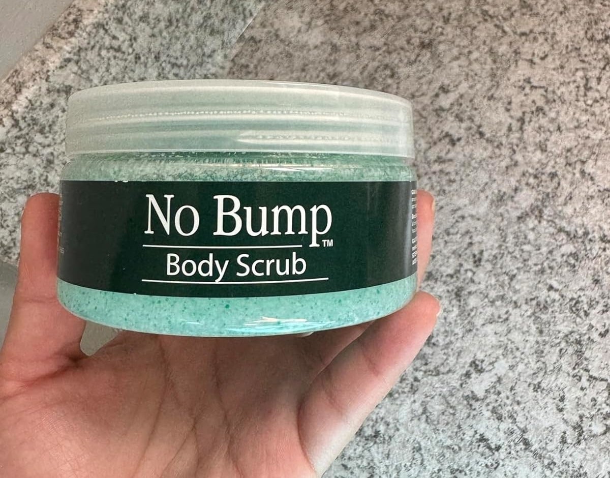 Reviewer&#x27;s photo of a hand holding a jar of &#x27;No Bump Body Scrub&#x27; against a marble counter background