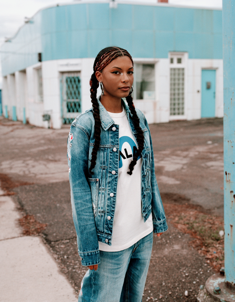 Woman in a denim jacket and graphic tee standing before a building