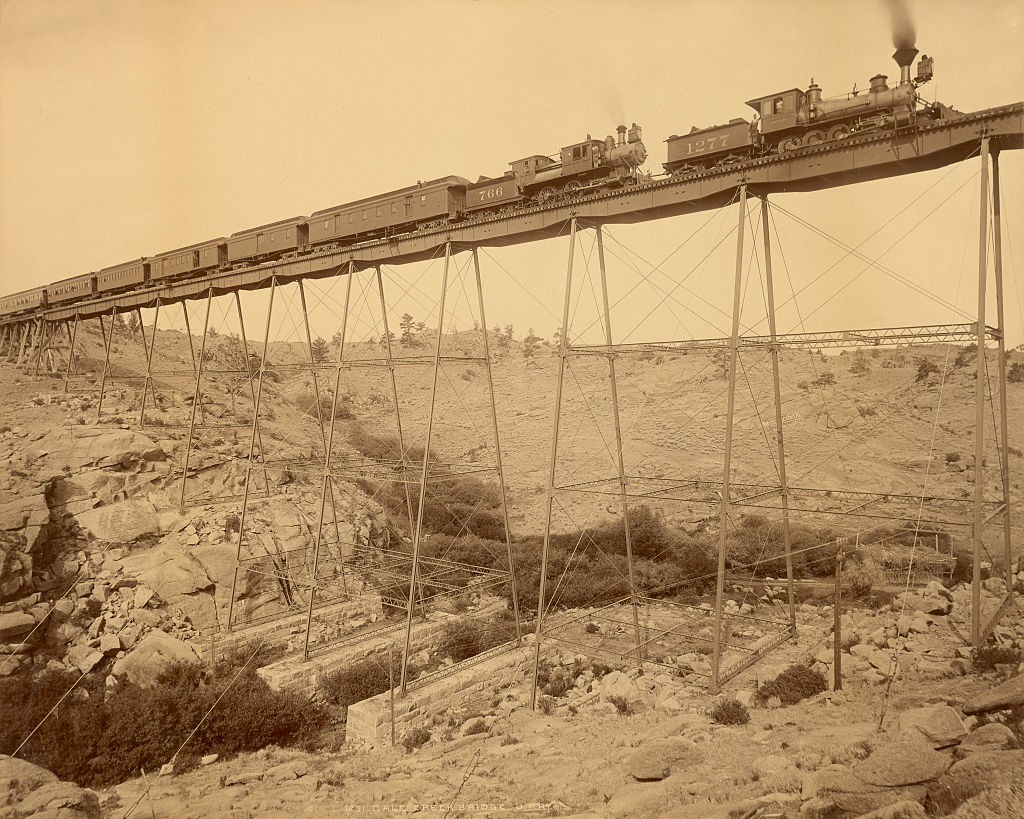 Old photograph of a steam train crossing a high trestle bridge over rocky terrain